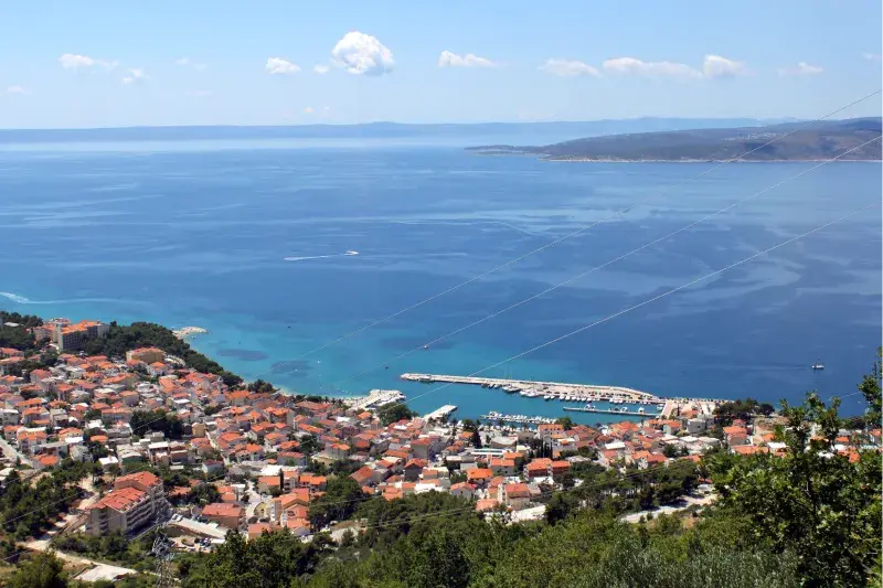 Appartements Baška Voda – vue panoramique sur le village côtier et la marina, la mer turquoise et Biokovo en arrière-plan.