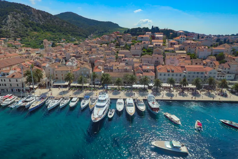 Apartmány Hvar – pohled na nábřeží starého města Hvar s luxusními jachtami, palmami a tradičními kamennými domy podél pobřeží Jaderského moře.