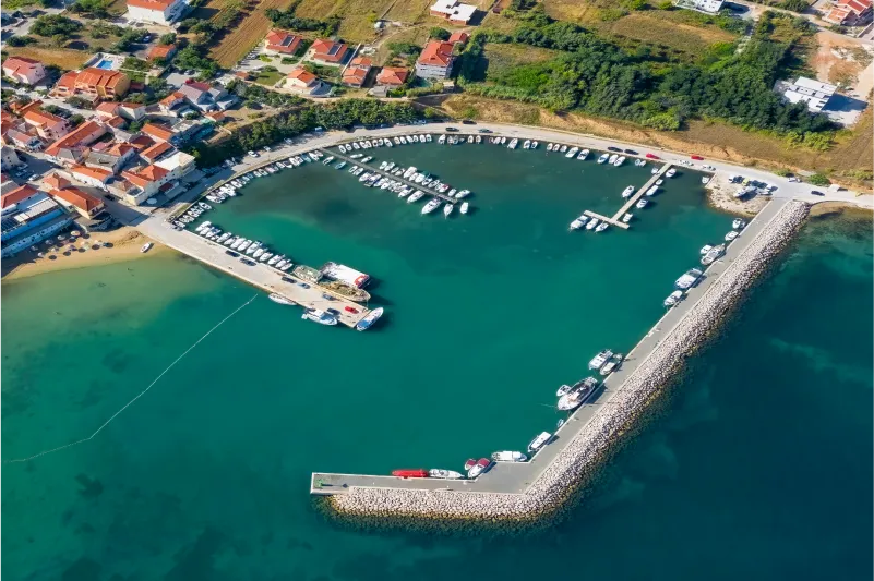 Apartamentos Privlaka: vista aérea de la bahía de arena y el puerto con barcos en el mar turquesa.