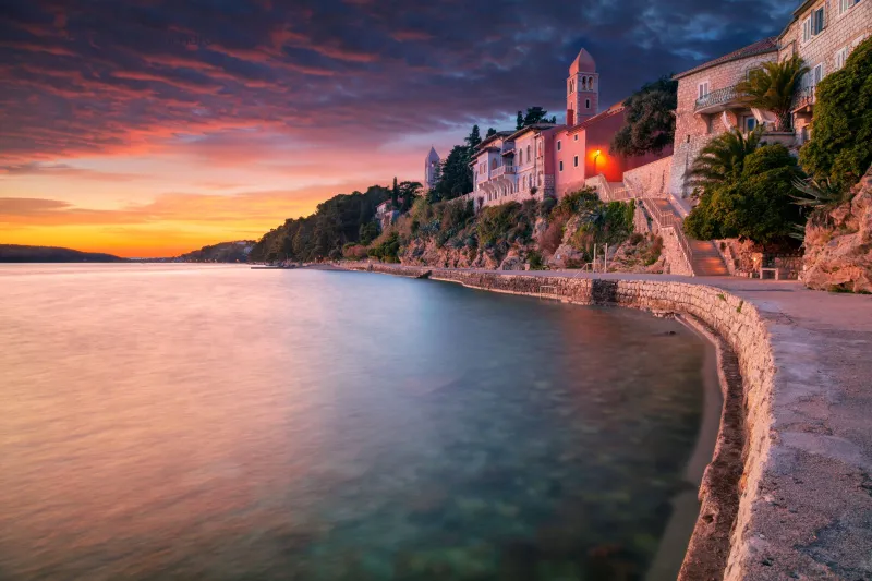 Rab apartmani – pogled na povijesne kamene kuće uz obalu grada Rab, mirno more i spektakularan zalazak sunca na otoku Rabu.