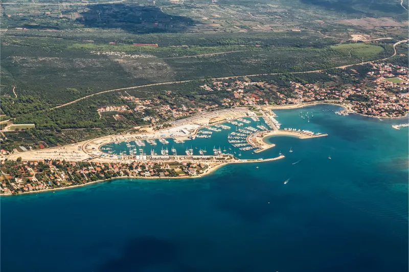 Apartamente Sukošan - Vedere aeriană a orașului Sukošan - un port plin de iahturi și bărci, o coastă cu promenadă și un sat înconjurat de verdeață și de Marea Adriatică.
