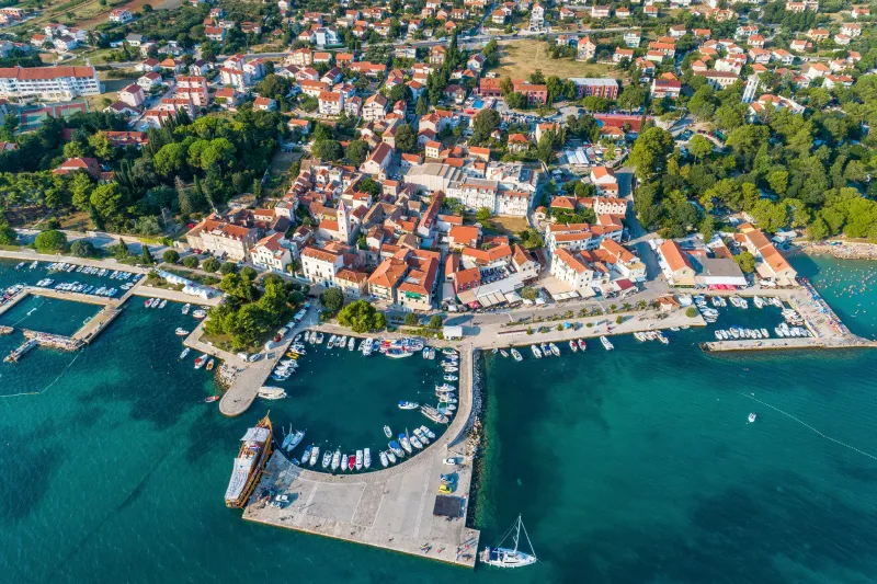 Lägenheter Sveti Filip i Jakov – Flygfoto över den pittoreska kuststaden med en marina, många båtar och röda tak längs det turkosa havets strand.