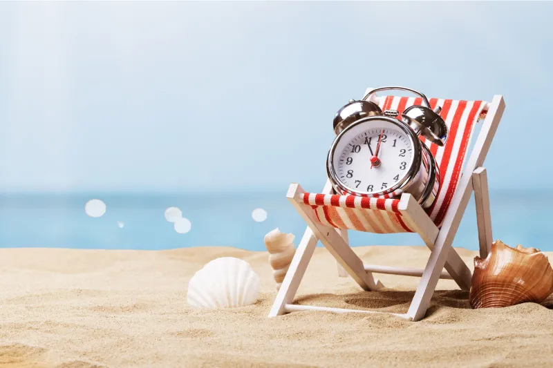 Een klok op een ligstoel op een zandstrand symboliseert een last-minutevakantie aan zee, met een achtergrond van blauwe lucht en schelpen in het zand.