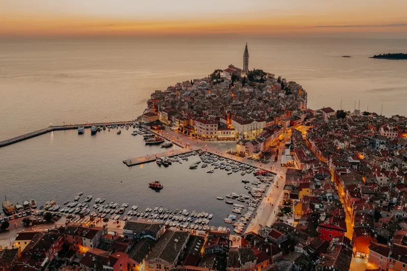 Rovinj leiligheter – panoramautsikt over Rovinj gamleby med kirken St. Eufemia, den opplyste promenaden full av båter og fargerike hus langs Adriaterhavskysten ved solnedgang.